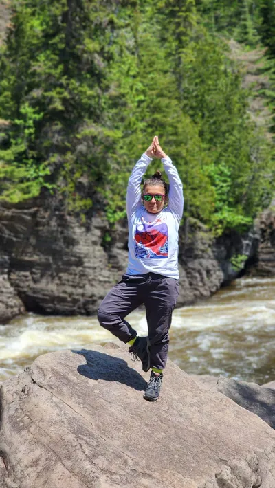 Lori in tree pose balanced on a rock, a river rushing behind her