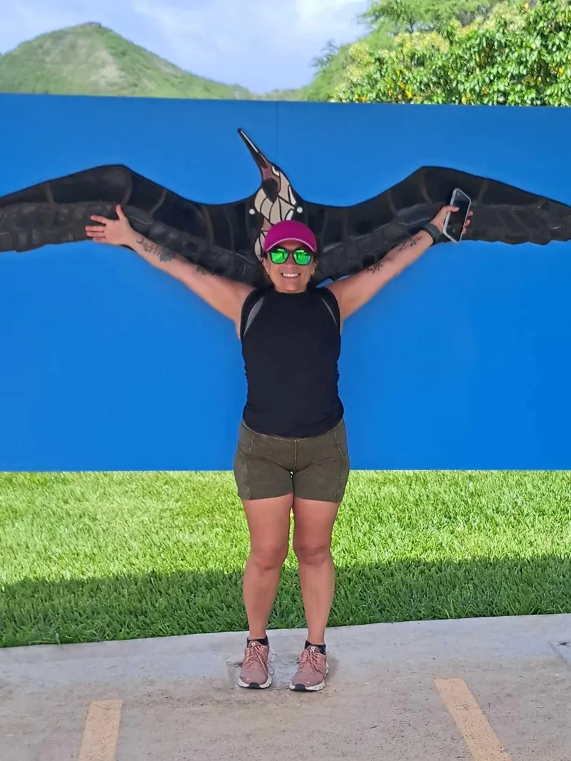Lori Schmidt spreading her arms beneath a native bird painting, welcoming and warm