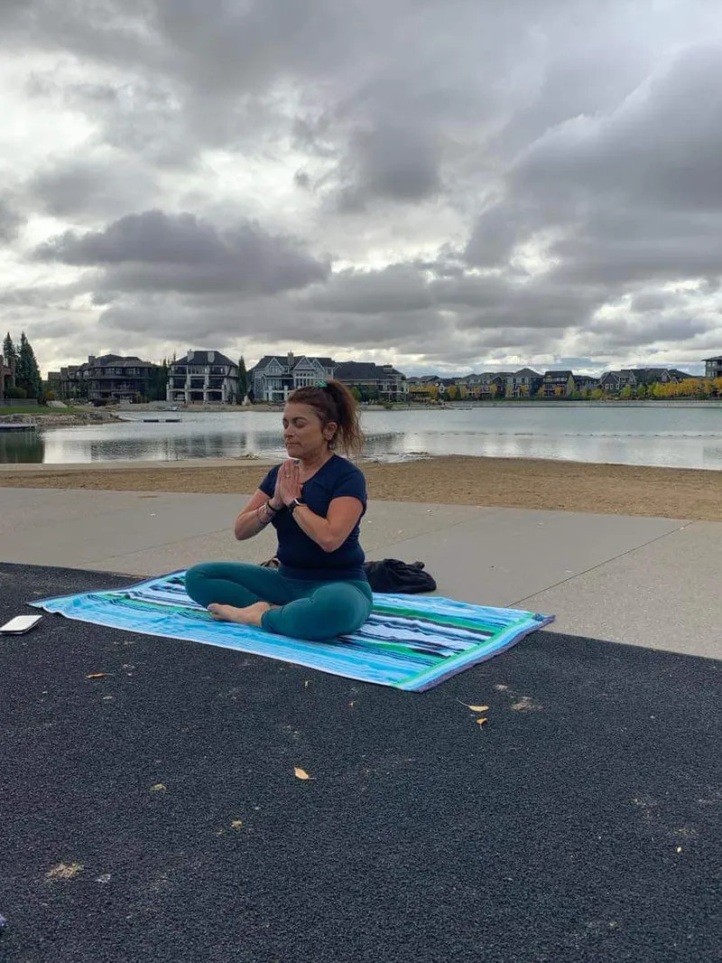 Lori Schmidt in seated meditation on a cliffside hiking trail, trees and skyline behind