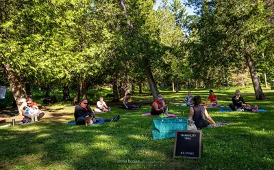 Lori guiding a small outdoor class, students on mats in a sunlit park